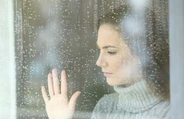 Frau mit leerem Blick hinter verregnetem Fenster - Hoffnungslosigkeit Depression
